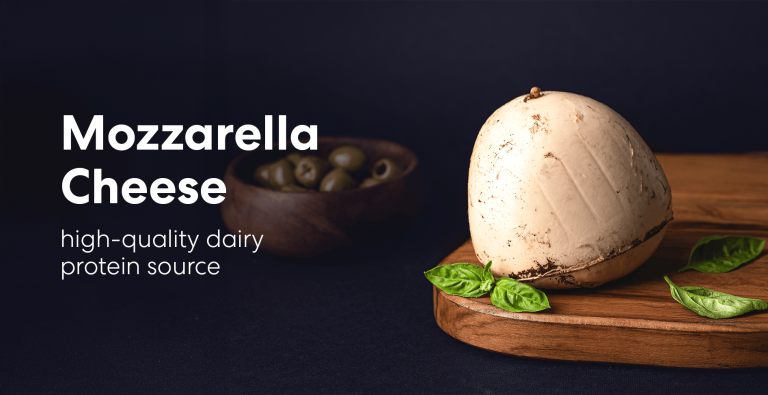 Fresh mozzarella cheese ball on a wooden board with basil leaves, against a dark background with olives in the background.